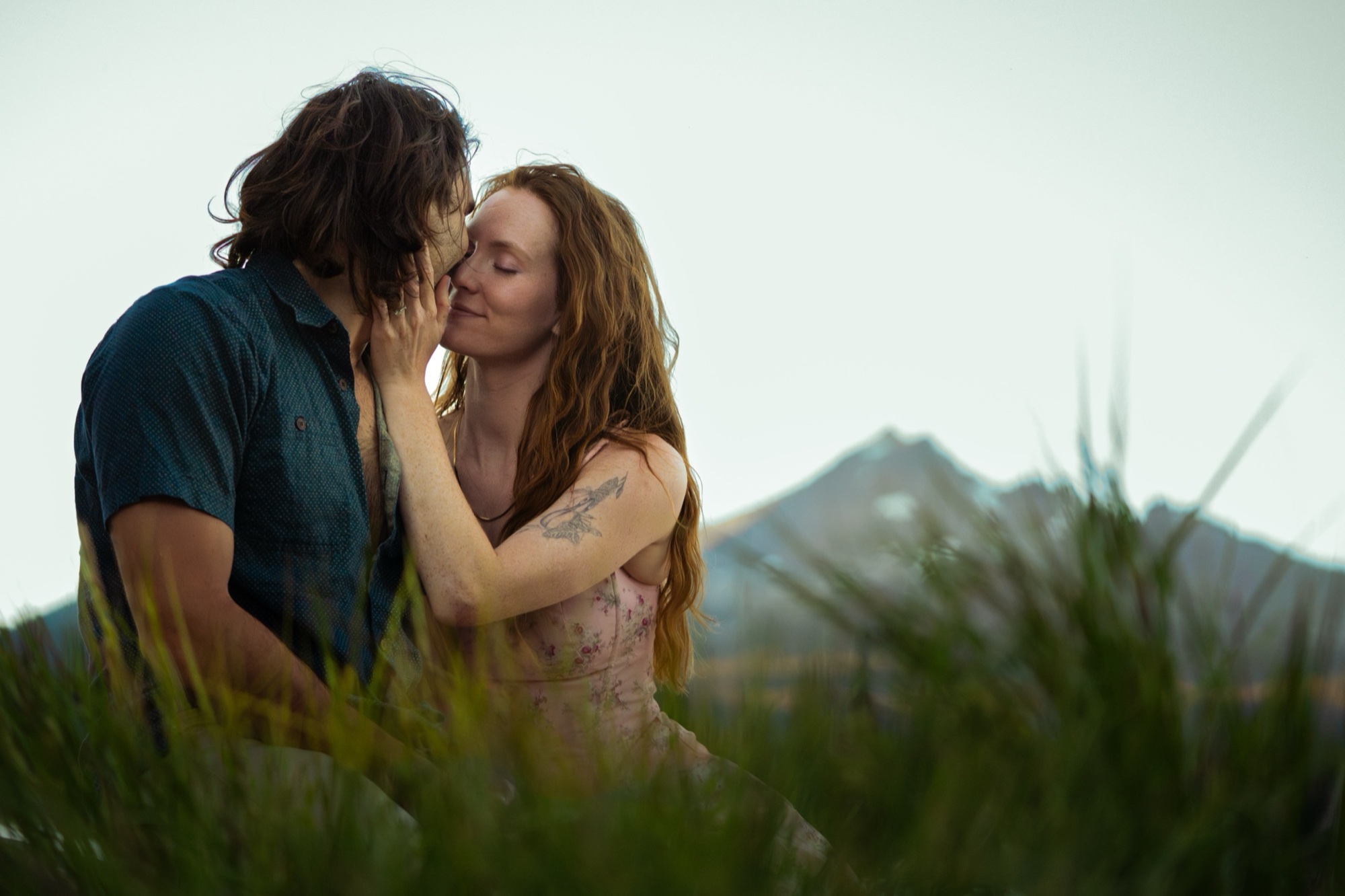 A couple close in tall grass, a mountain peak behind them.