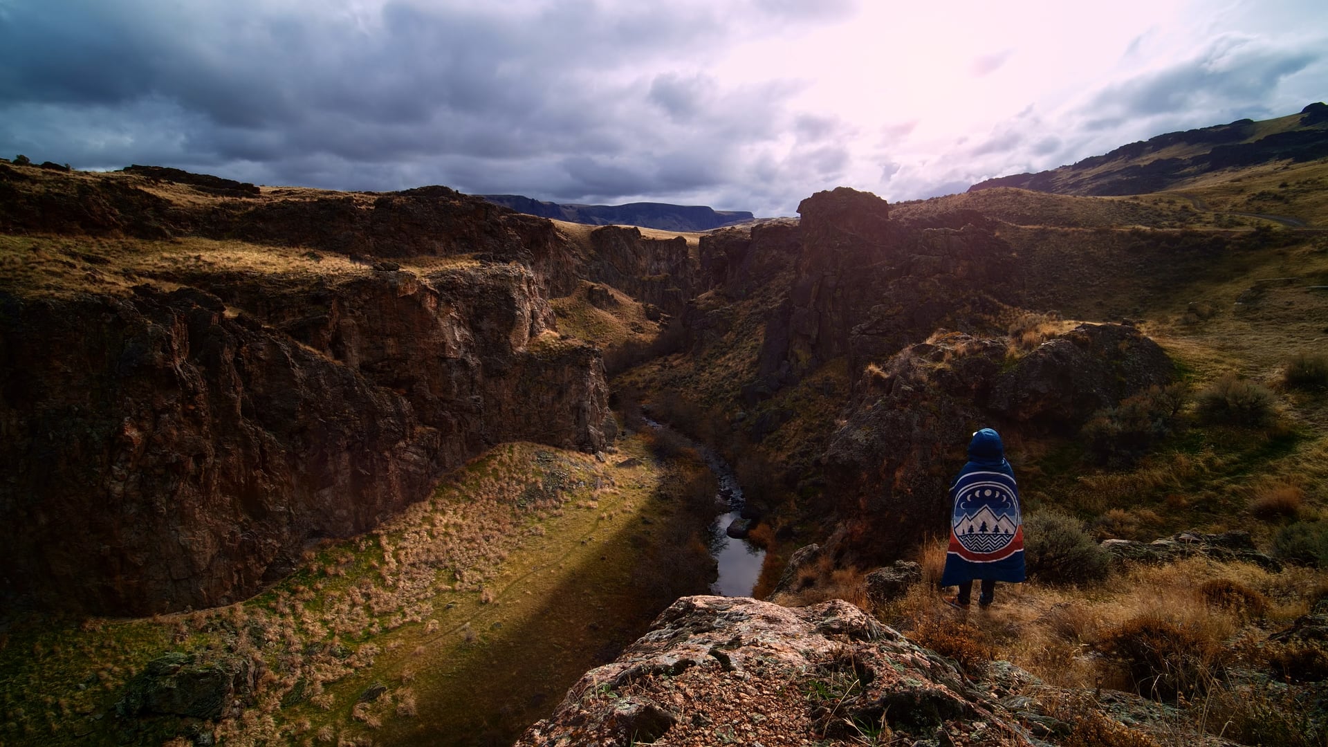 A lone figure on a canyon rim under heavy cloud.